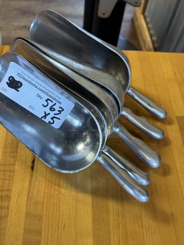 Five metal scoops, 24 oz capacity, stacked with visible auction tag, in used condition on a wooden surface.