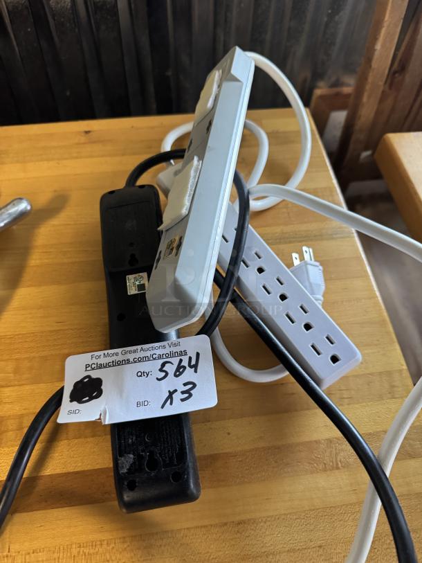 Three power surge cords in mixed condition with visible wear. Auction tag reads "Qty: 564 x3."