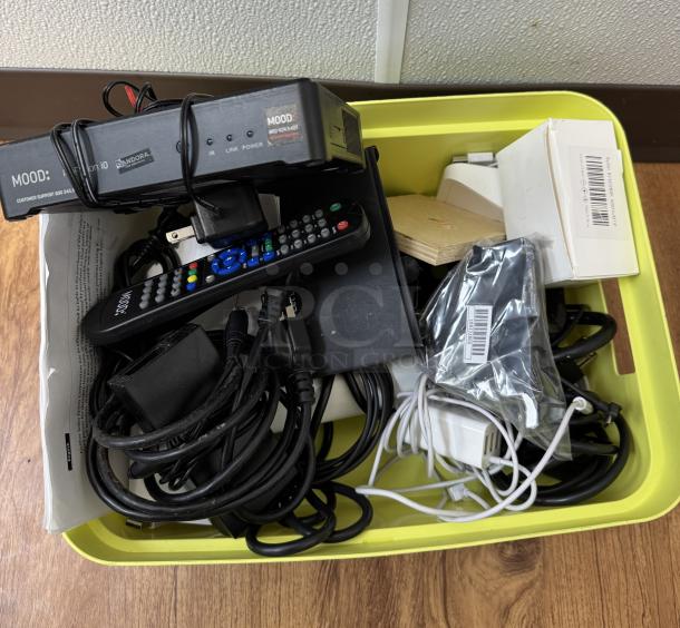 Assorted cables, cords, and chargers in a yellow bin. Includes a Mood remote, multiple power adapters, and various electronic cords.