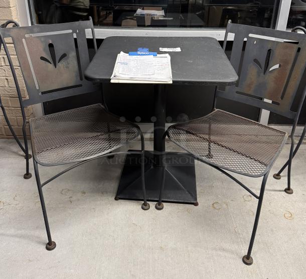 Metal table with two matching chairs, black finish, lattice seat design, decorative backrest cutout, in fair condition.