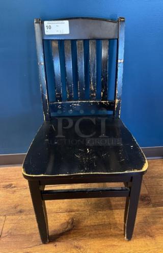Black wooden dining chair with distressed finish, slatted back, and number tag. Visible wear adds vintage appeal.