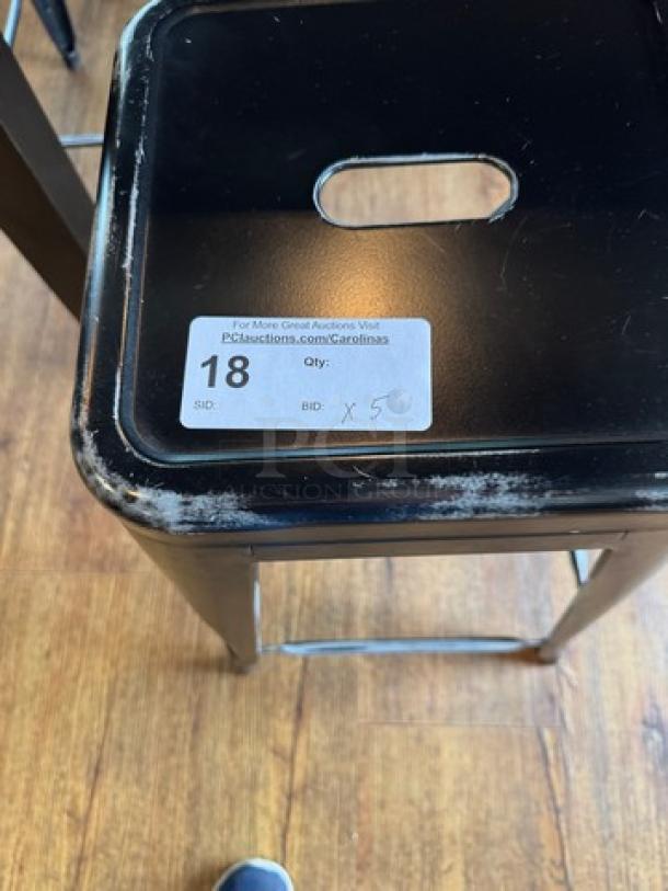 Black metal stool with a square seat, featuring visible wear on edges. Auction tag shows lot number 18 and bid quantity x5.
