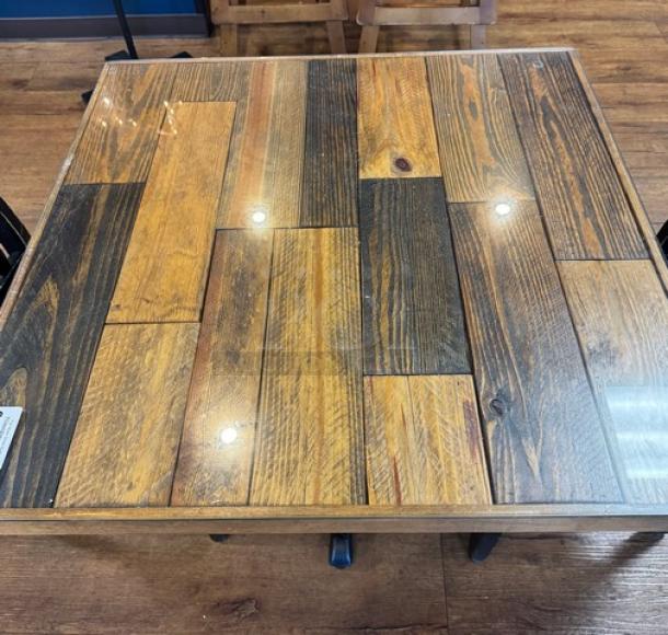 Wooden dining table with a glass top, featuring a rustic wood panel design. Excellent condition, square shape, no visible labels.