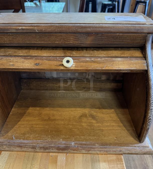 Wooden decorative bread box with a roll-top lid, showing signs of wear. Features simple design and compact size.