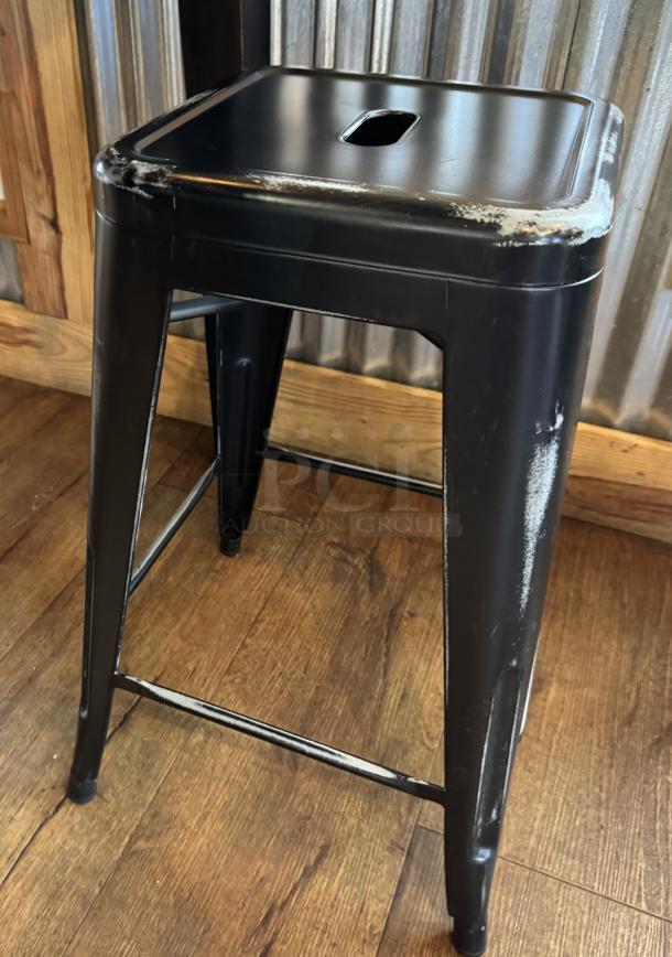 Black metal stool, model b, with visible wear and scuffs on edges.