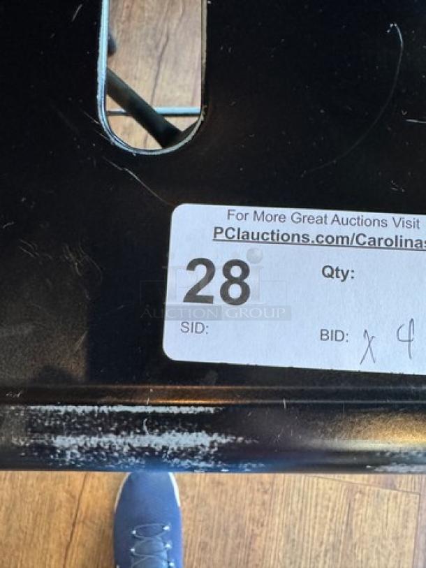 Black metal stool with auction label showing item number 28 and bid quantity x4; slight wear visible on surface.
