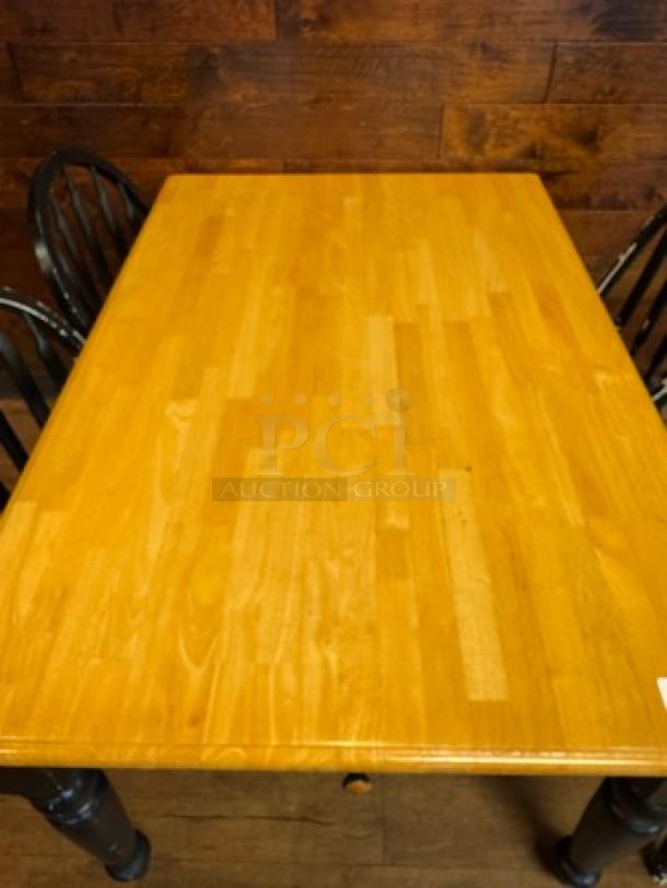 Wooden dining table with a light finish, rectangular shape, black legs. Slight wear visible. Ideal for contemporary decor.