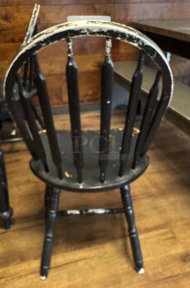 Set of four black wooden dining chairs, vintage style with noticeable wear and distressed finish, featuring spindle backs.