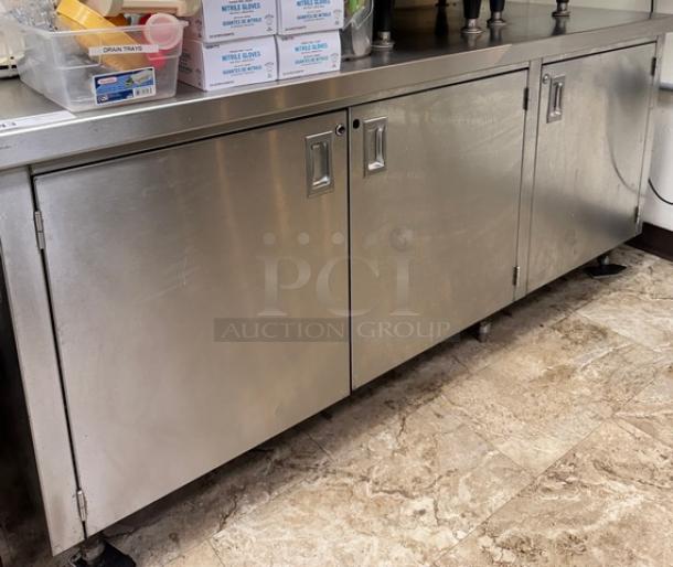 Stainless steel equipment stand with storage, featuring three cabinet doors and a durable top surface. Appears in good condition.