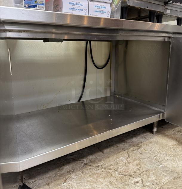 Stainless steel equipment stand with storage shelf, minor wear, ideal for kitchens, durable construction, visible cords above.