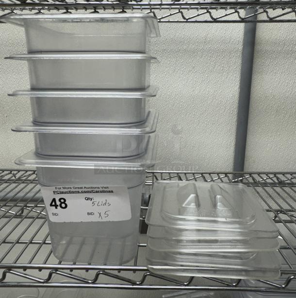 Vigor stainless steel 1/6 x 6 pans with lids, set of 5. Pans and lids stacked on a metal shelf. Auction tag reads "Qty: 5 Lids x 5."