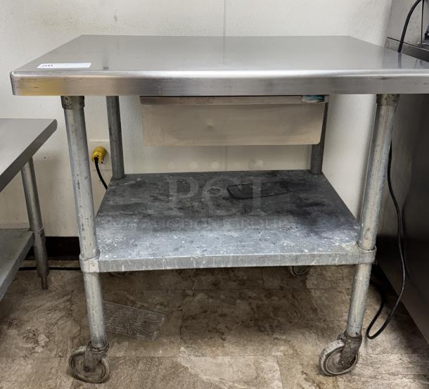 Stainless steel equipment stand with drawer, galvanized shelf, on casters. Shows signs of wear, ideal for kitchen use.