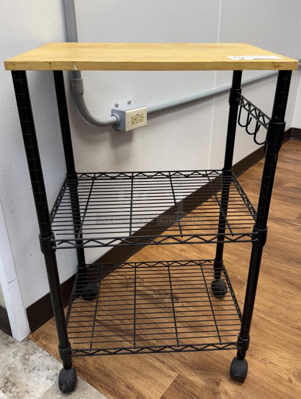 Rolling display/storage cart with wooden top, two wire shelves, and wheels. Black metal frame, used condition.