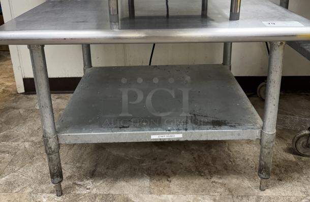 Stainless steel equipment stand with undershelf, showing signs of wear. Tag reads "STAFF DRINKS".