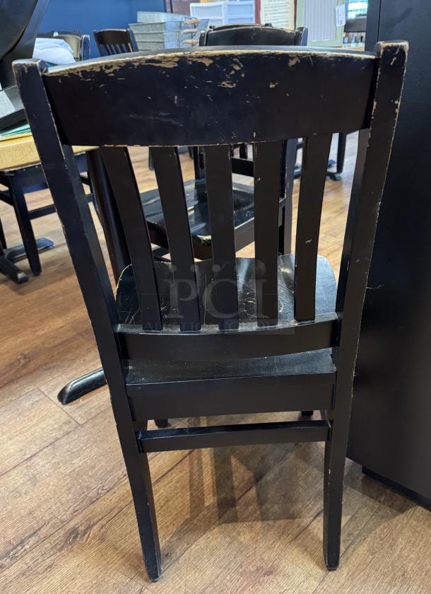 Set of 4 black wooden dining chairs with slatted backs, showing signs of wear with scratches and scuffs.