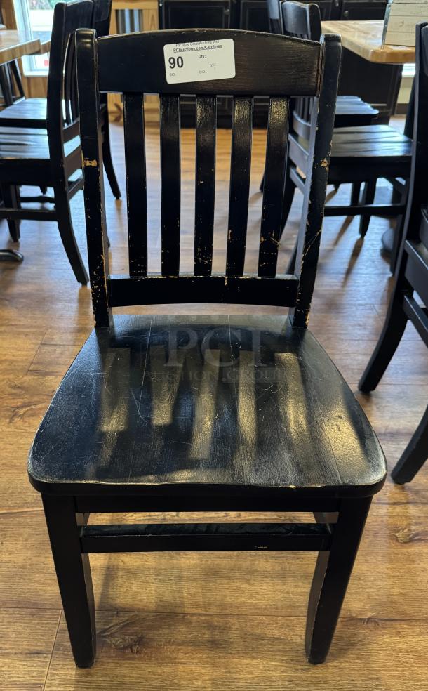 Four black dining chairs with slatted backs, showing signs of wear. Auction tag "90" visible on backrest.