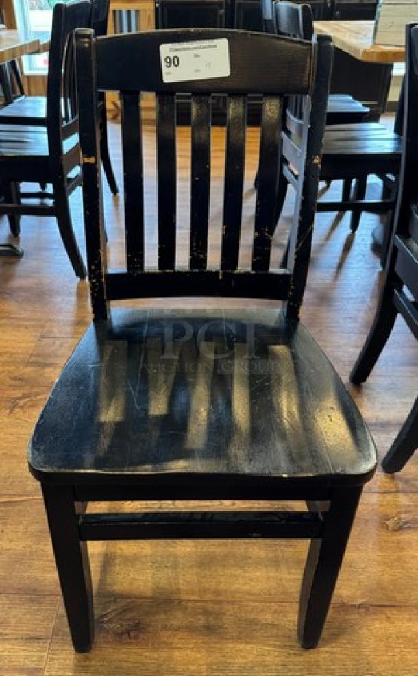 Black wooden dining chair with vertical slat backrest. Visible wear and scuffs. Auction tag displays number 90.