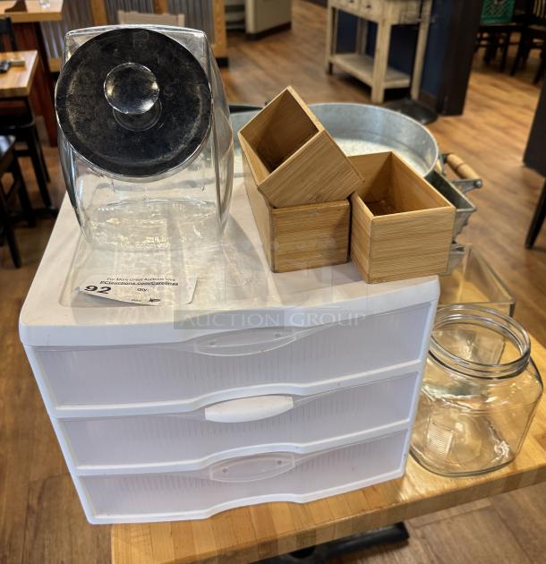 Assorted storage containers including plastic drawers, bamboo boxes, and glass jars. White plastic drawers marked "Sterilite."