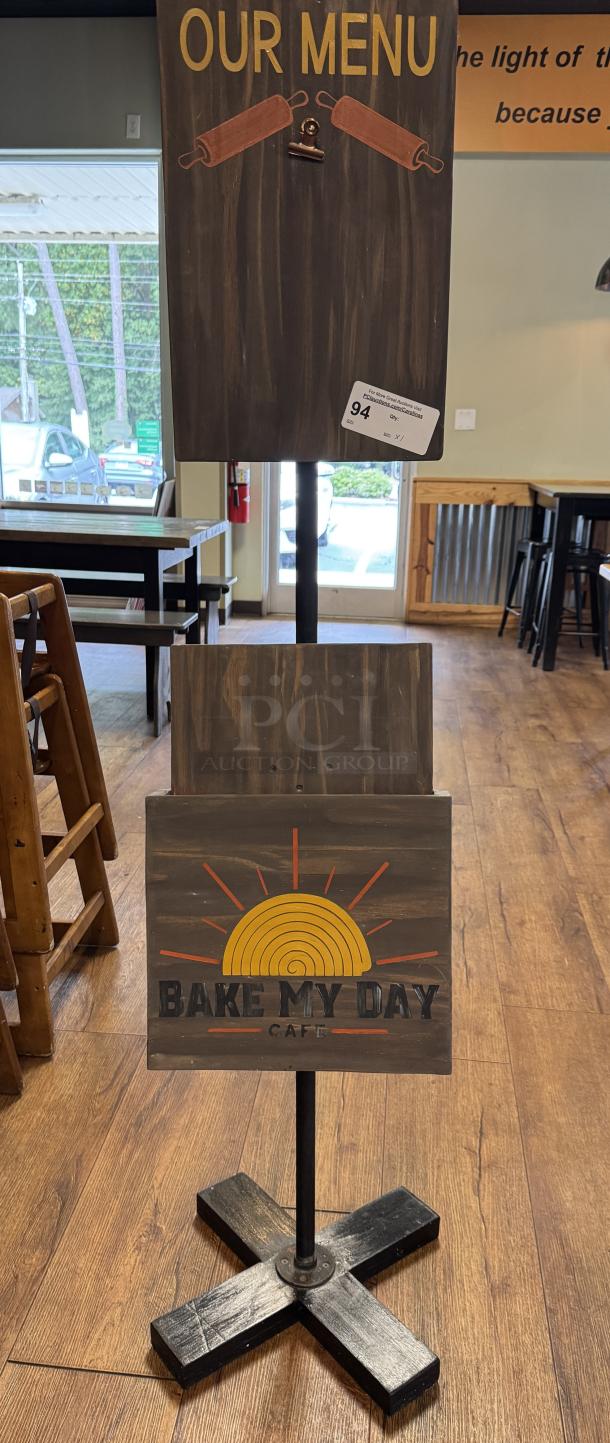 Decorative wooden floor sign with "Our Menu" and "Bake My Day Cafe" logos. Dark wood finish, sturdy black base. Auction tag visible.