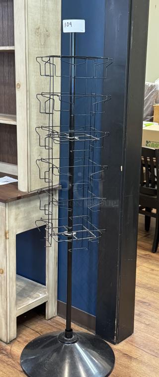 Metal floor magazine rack with multi-tiered wire baskets, black finish, sturdy round base, and labeled "104".
