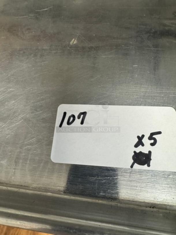 Full size sheet pans, lot of 5. Stainless steel, used condition, visible wear. Tag reads "107 x5."