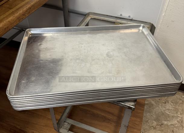 Stack of 10 full-size aluminum sheet pans, used condition, showing surface wear, ideal for commercial baking.