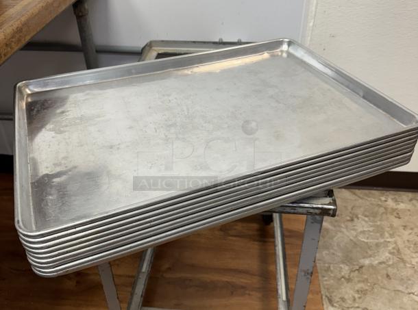 Stack of 10 full-size aluminum sheet pans, used condition, visible wear. Great for baking or cooking in bulk.