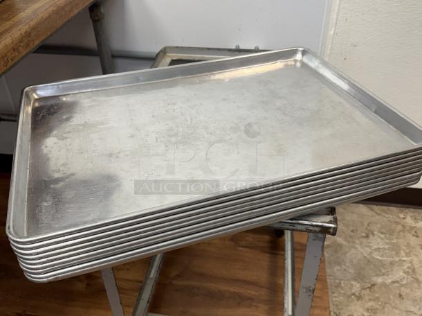 Full-size sheet pans stack, 10 count, aluminum, used condition, smooth surfaces, suitable for baking or roasting.