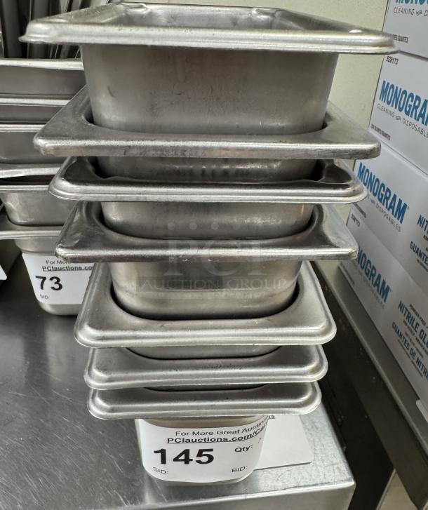 Stack of seven stainless steel rectangular pans, size 1/6 x 4. Visible auction tag shows quantity as 7, bid number 145.