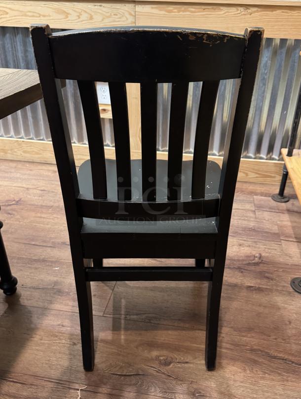 Black wooden dining chair with slatted back, showing wear on edges. Available as set of four.