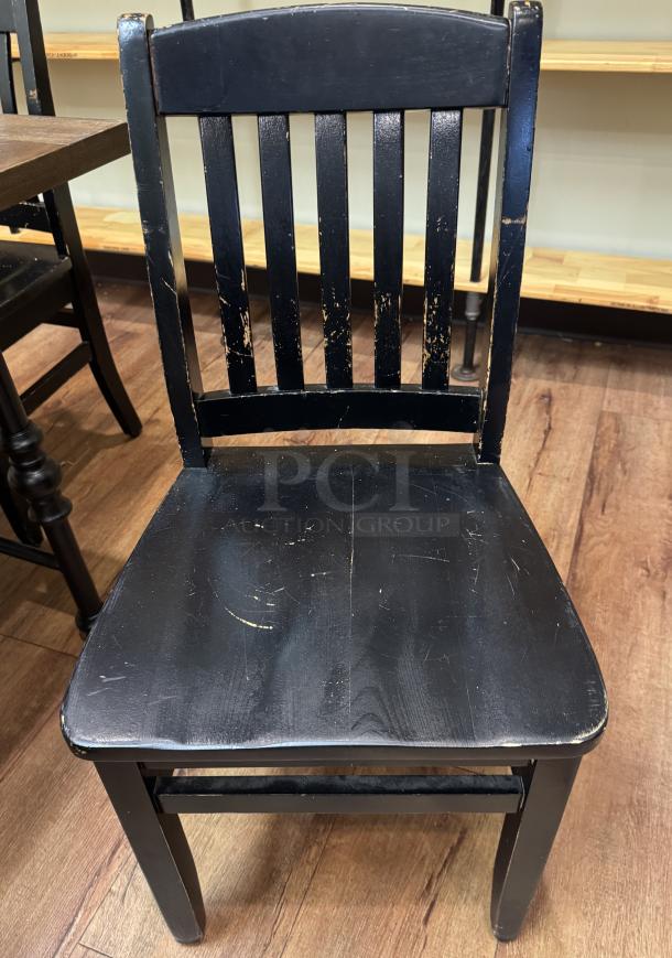 Black dining room chair with slatted back, visible wear, and scratches. Vintage look. Part of a set of four chairs.