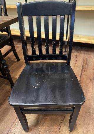 Black dining room chair with slatted back, visible wear, and scratches. Vintage look. Part of a set of four chairs.