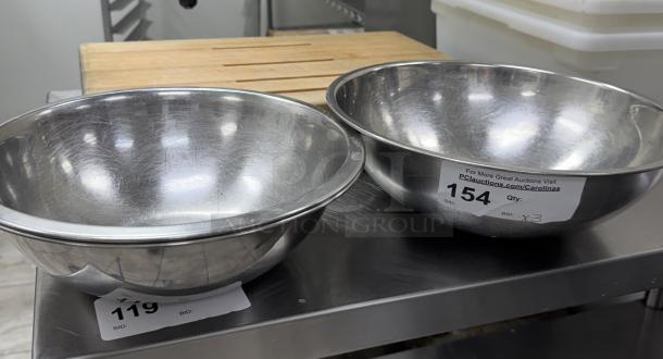 Three stainless steel mixing bowls with a reflective finish, visible auction tags 119 and 154. Quantities stated: 3. Scratches present.