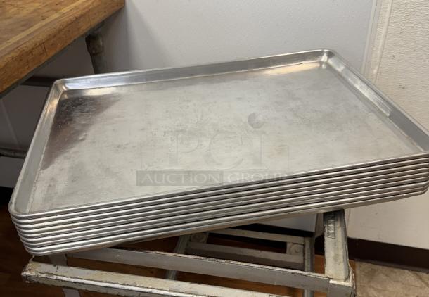 Stack of 10 full-size aluminum sheet pans, lightly used, ideal for commercial baking. No visible labels or markings.
