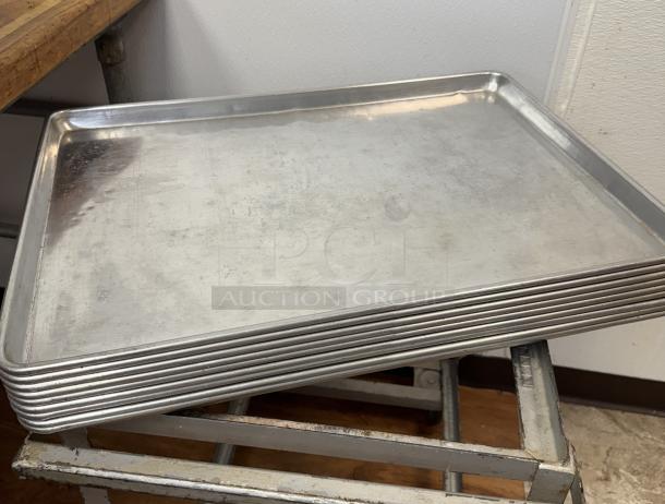Full-size sheet pans, 10 pieces stacked, metal, used condition. Ideal for commercial baking, sturdy construction.