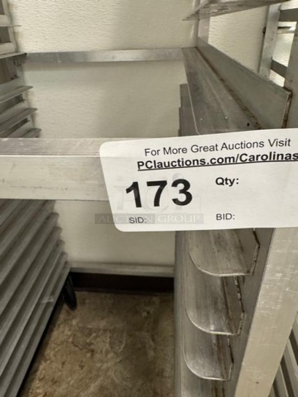 Metal rolling sheet pan rack with multiple shelves, silver finish, auction tag numbered 173 visible. Suitable for bakery use.