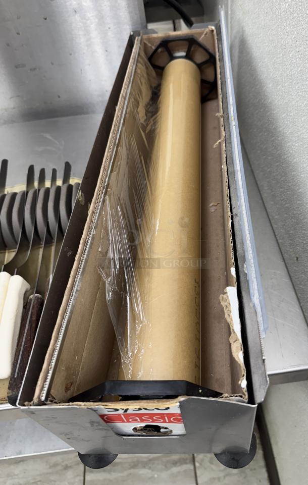 Metal plastic wrap holder with cutter, featuring roll of wrap inside, labeled "Classic" on side, in used condition.