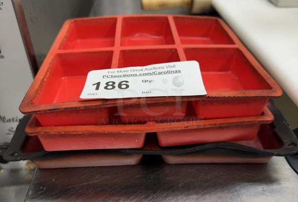 Red silicone baking molds, set of three, each with six square compartments. Minor signs of use. Auction tag reads "186".