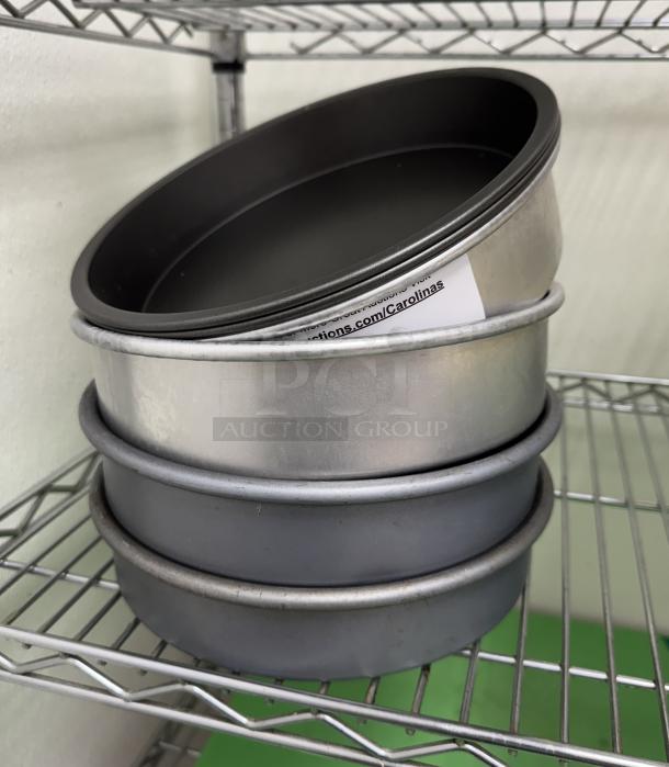 Assorted metal cake pans, stack of four, various finishes, on a metal shelf. Includes an auction tag inside.