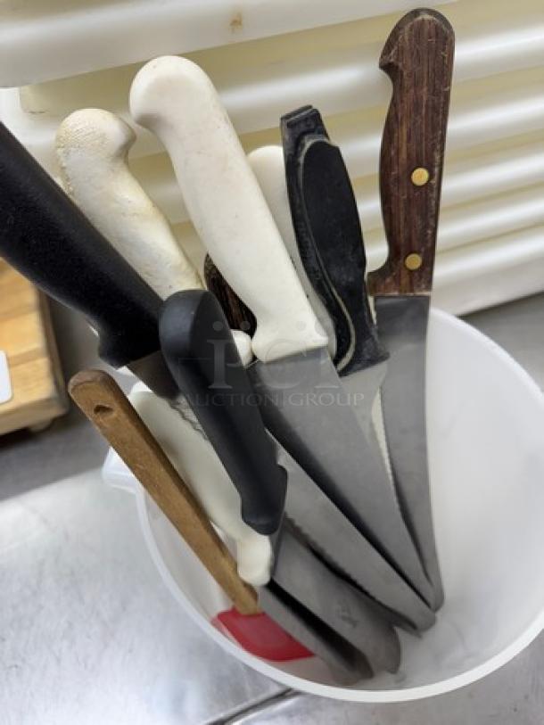 Assorted knives and spreaders in a white container, featuring various handles in black, white, and wood. Mixed condition.