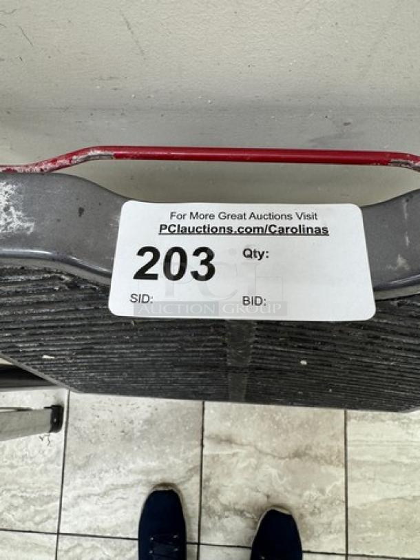 Gray metal step stool with a textured surface and red handle. Auction tag reads "203" with a link to PCauctions.com/Carolinas.