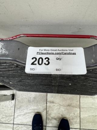 Gray metal step stool with a textured surface and red handle. Auction tag reads "203" with a link to PCauctions.com/Carolinas.