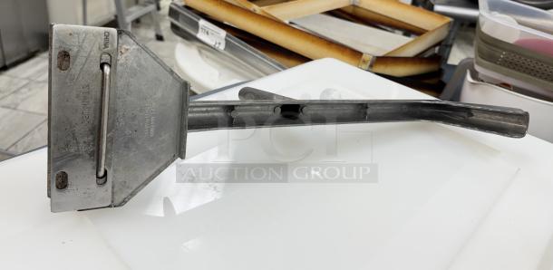 Metal grill scraper with long handle; marked "Made in China" and "Stainless Steel"; used condition, slight rust visible.