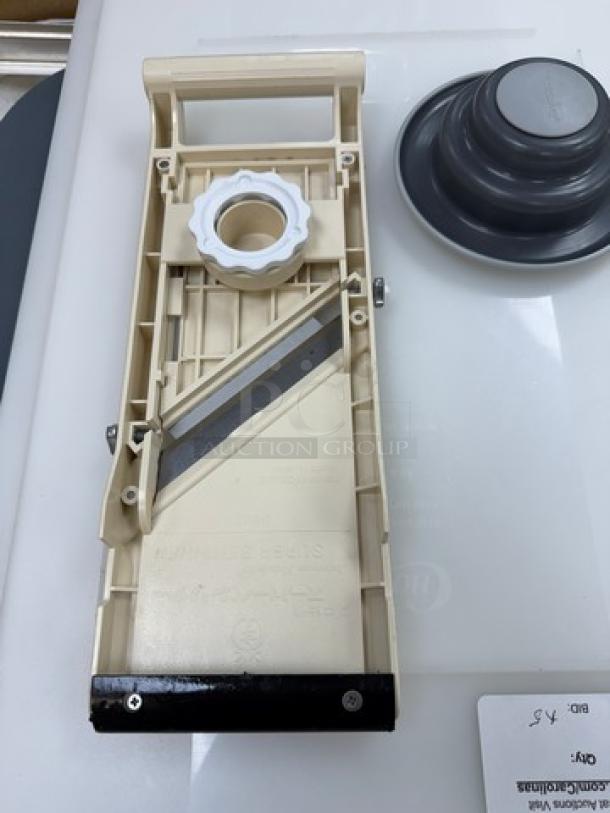 Plastic and metal mandolin slicer with adjustable blade, white and black. Includes a food holder. Model and brand markings visible.