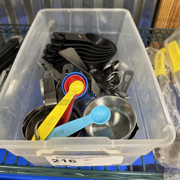 Assorted measuring cups and spoons in a plastic bin; includes colorful plastic and metal sets, clearly labeled for sizes.