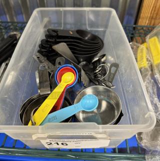 Assorted measuring cups and spoons in a plastic bin; includes colorful plastic and metal sets, clearly labeled for sizes.