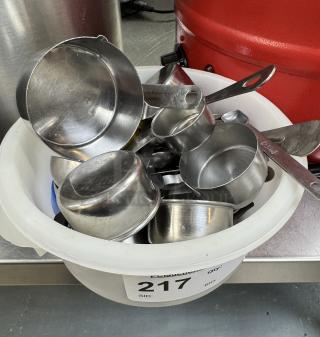 Assorted metal measuring cups and spoons in a white container, auction tag 217, in good condition.