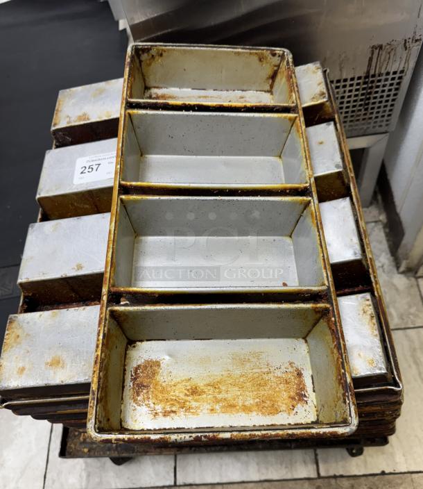 Twelve metal bread pans with rust and wear, stacked. Label marked "257.” Used condition.