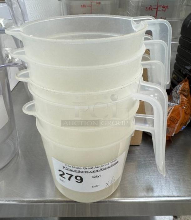 Stack of six 4-cup measuring cups with clear plastic handles, marked "279" and "qty: x6" tag for auction.