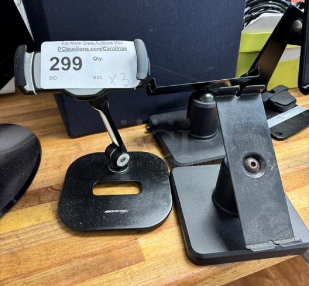 Three AboveTEK iPad holders on wooden surface, including base plates and adjustable arms. Visible label reads "299, Qty: x3".